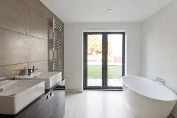 Modern bathroom with double sinks, a freestanding bathtub, and a glass door leading outside.