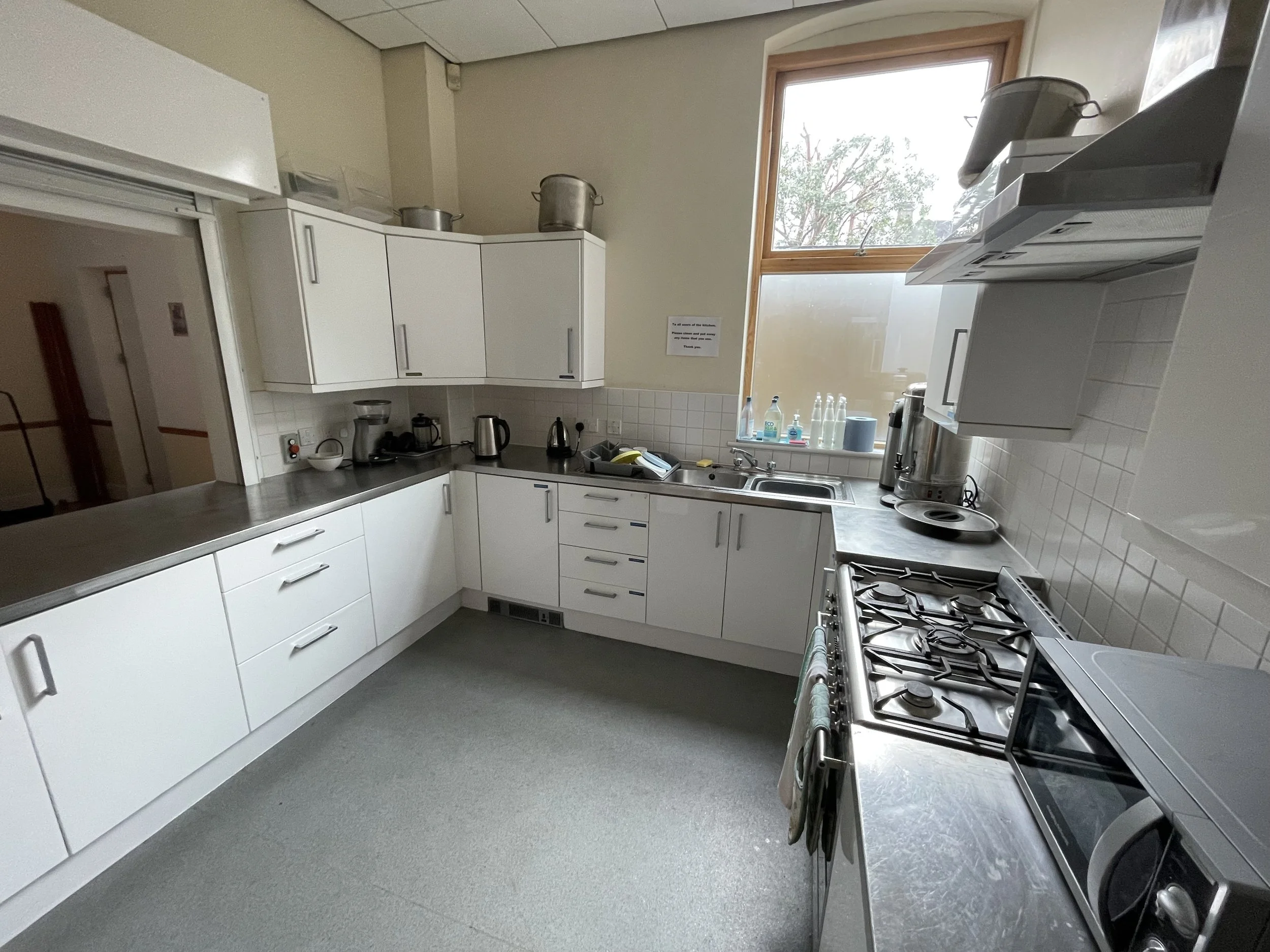 Empty kitchen with white cabinets, gray countertops, a stove, microwave, and window with trees outside.