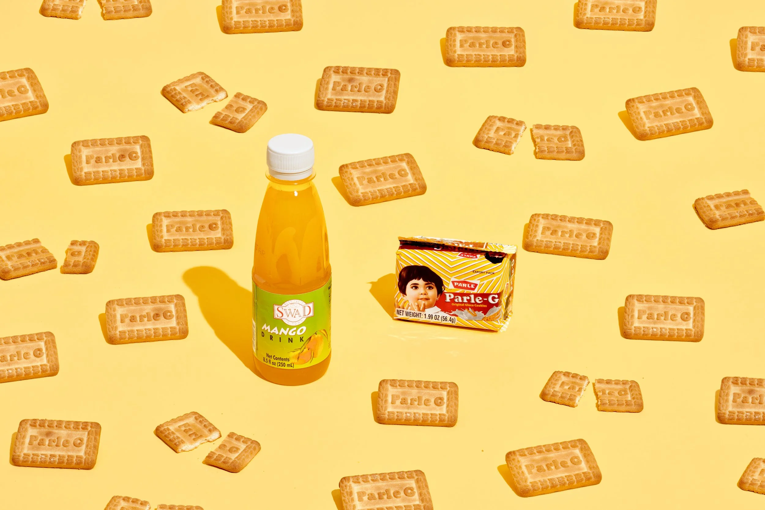 A yellow background with scattered rectangular biscuits with the word 'Parle G' stamped on them, a bottle of mango drink, and a pack of Parle G cookies featuring a child's face.