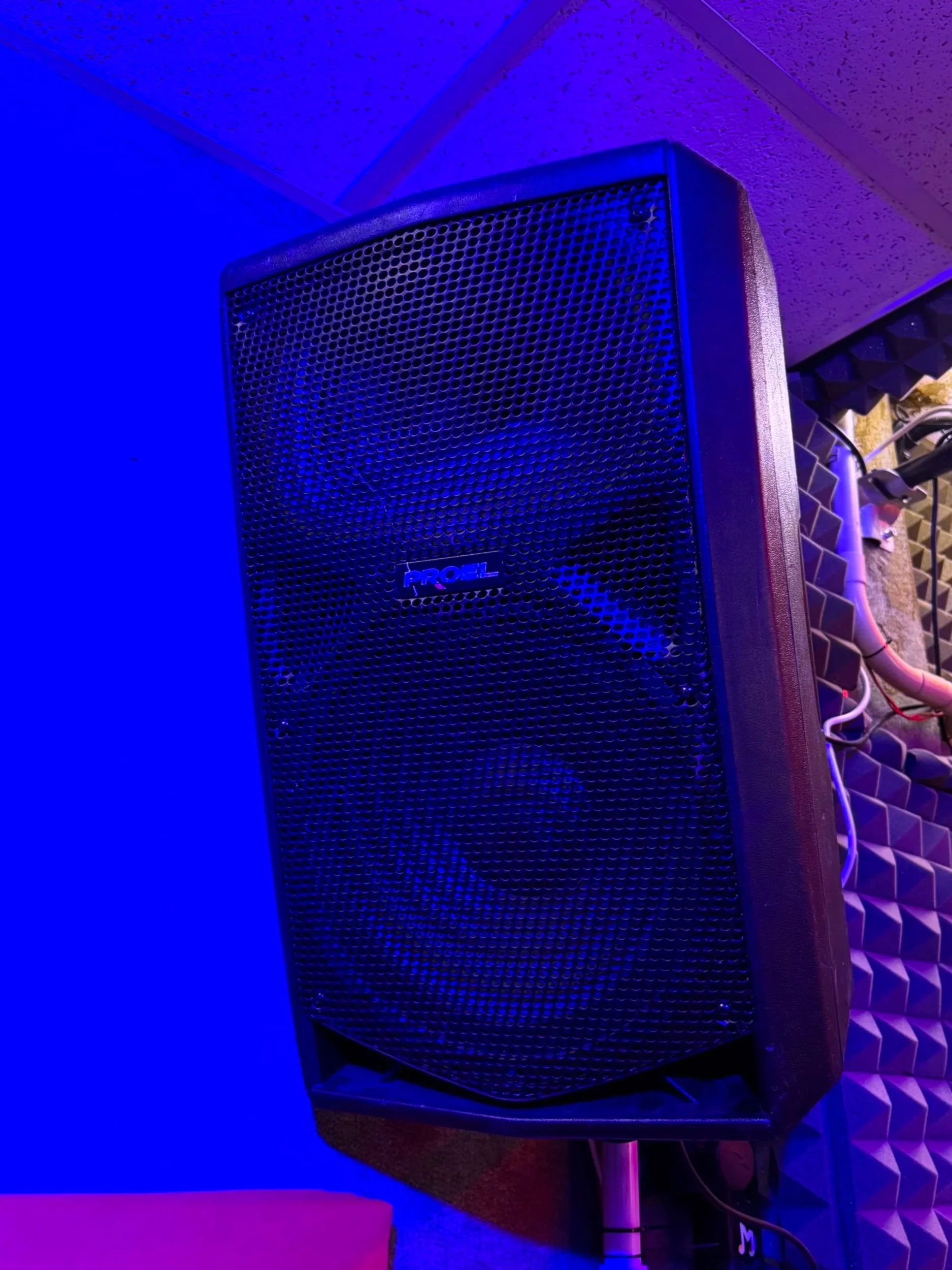 Altoparlante nero in un ambiente con illuminazione blu e sfondo con pannelli acustici.