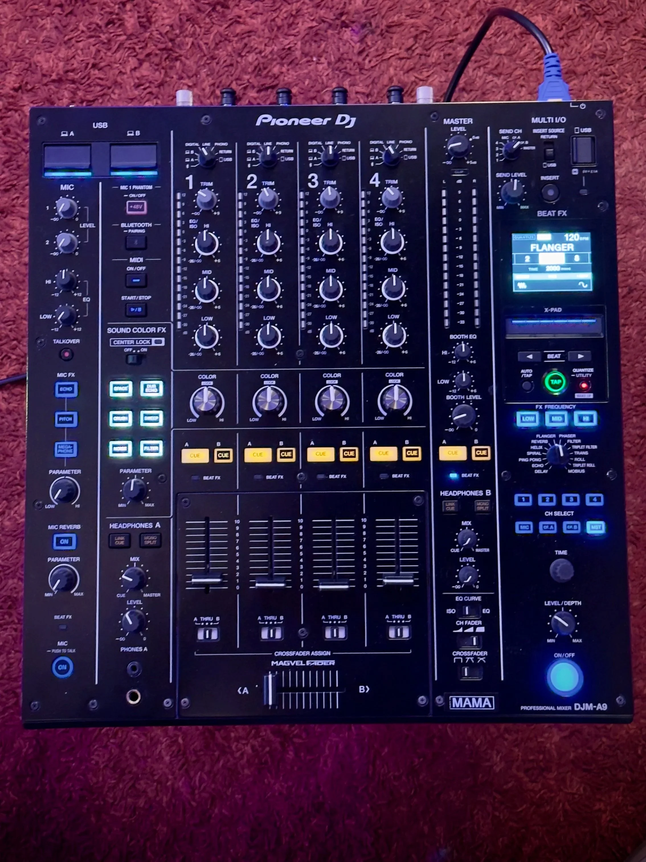 Mixer audio Pioneer DJ DJM-A9 con display acceso e vari controlli, posizionato su tappeto rosso.