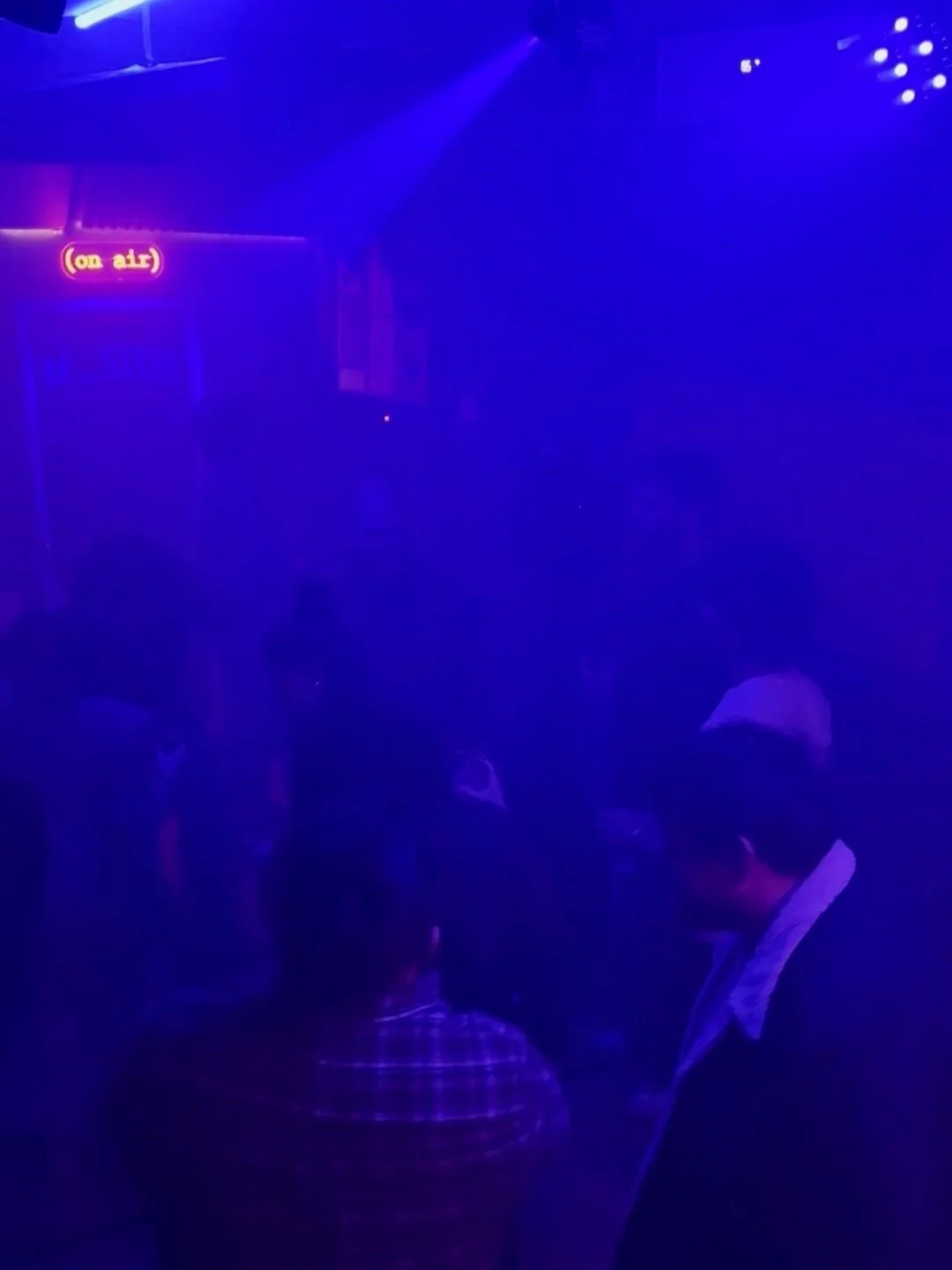 Immagine di una scena al buio con luci blu e un segno luminoso che dice '(on air)'.