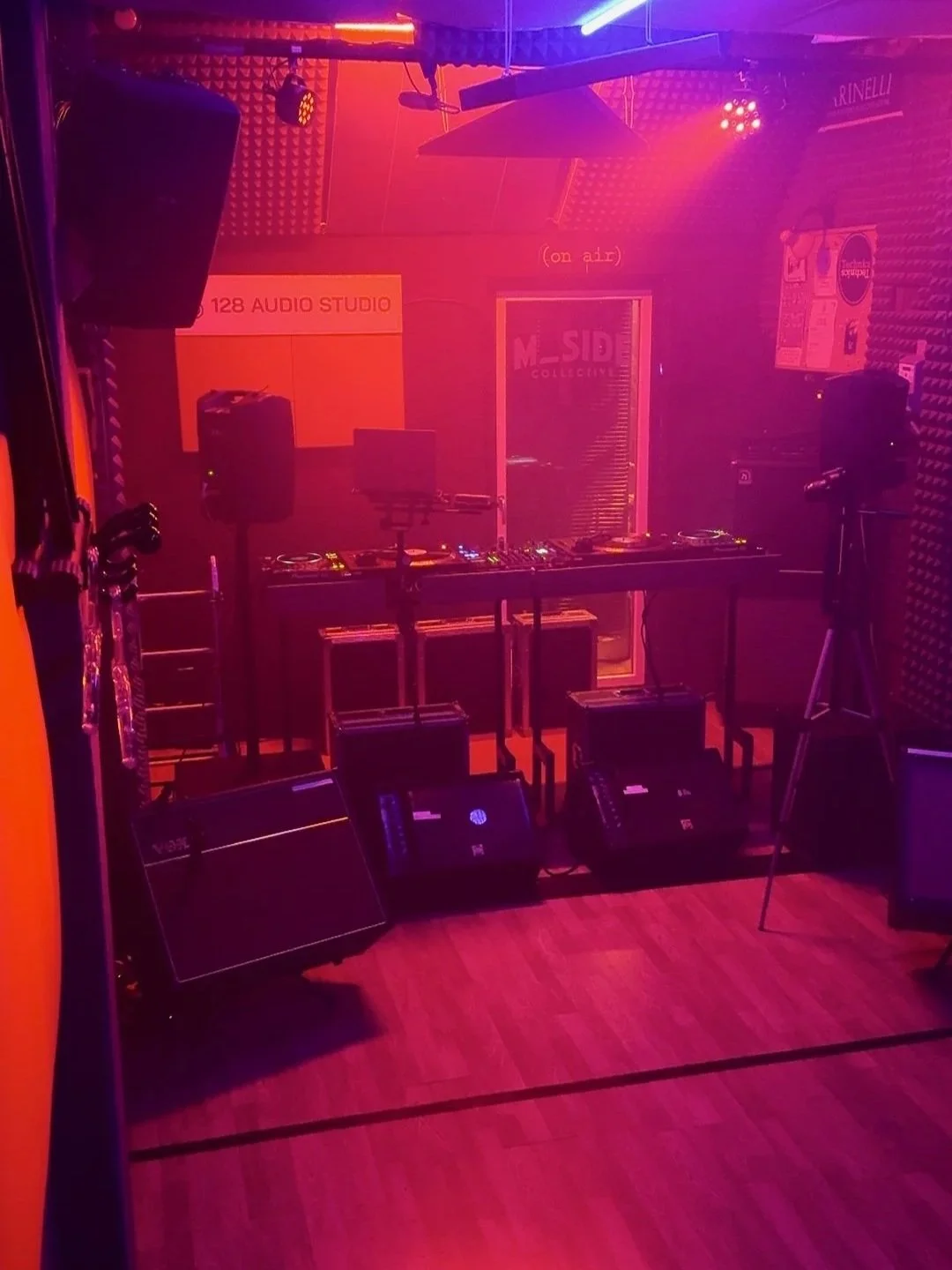 Studio di registrazione audio con DJ set up, luci soffuse e pareti rivestite con pannelli acustici in schiuma, attrezzature audio e da Dj.