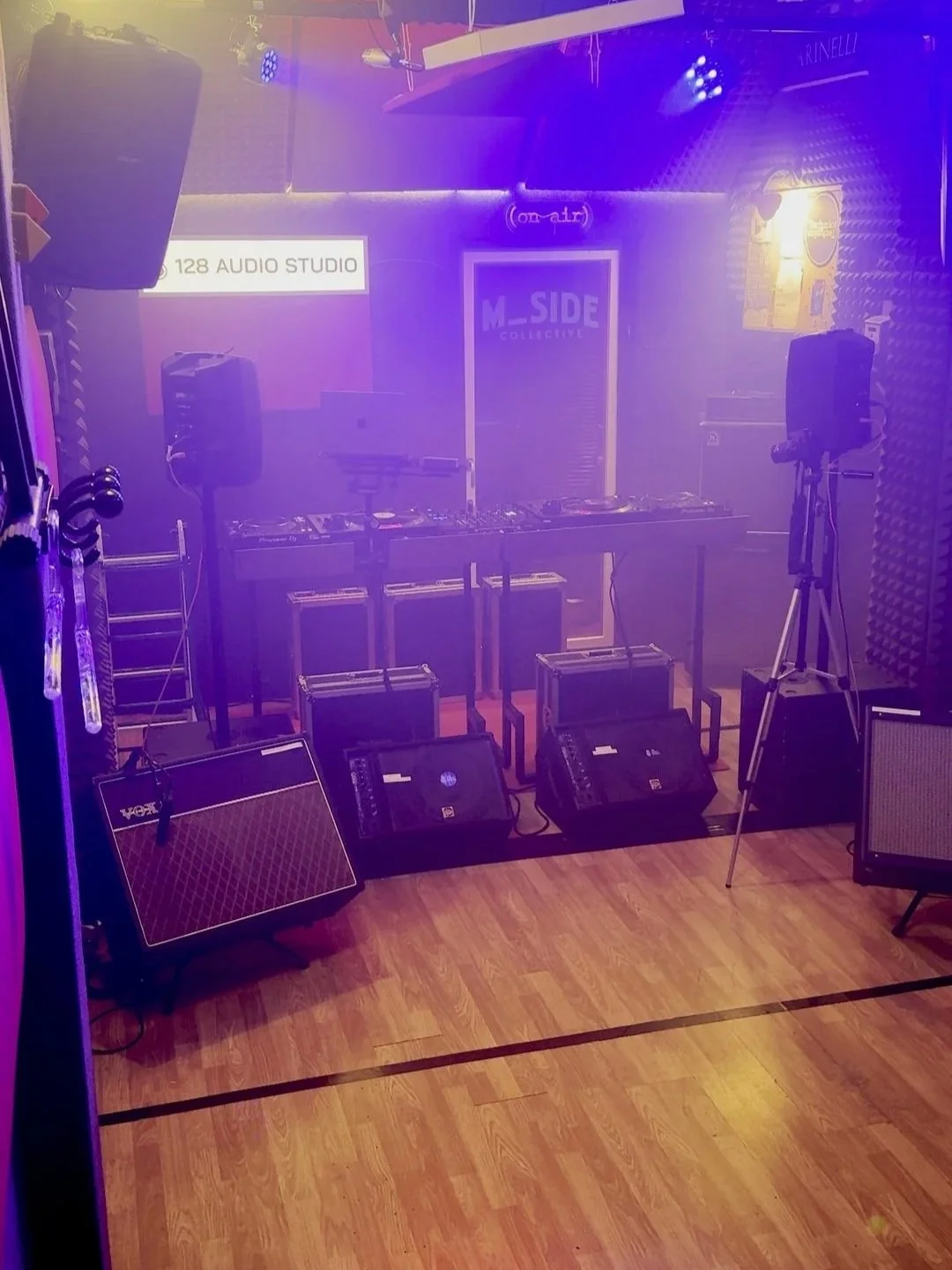 Stanza di registrazione audio con strumenti musicali, mixer, consolle DJ,  altoparlanti, microfoni e luci in tonalità viola e blu.