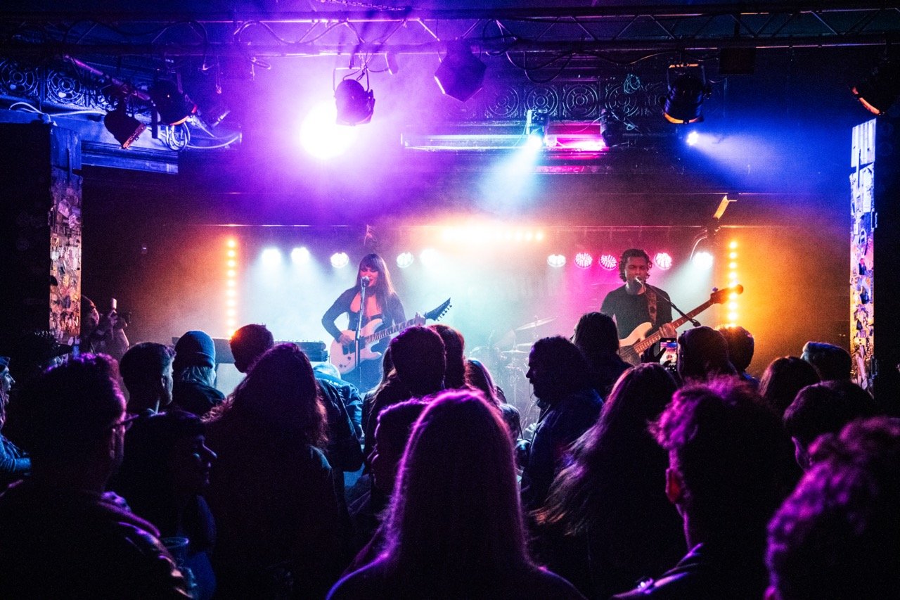 Calva Louise. A live music performance on stage with a female with guitar and a male with bass guitar, under colorful stage lights, in front of an audience at Bedford Esquires concert venue.