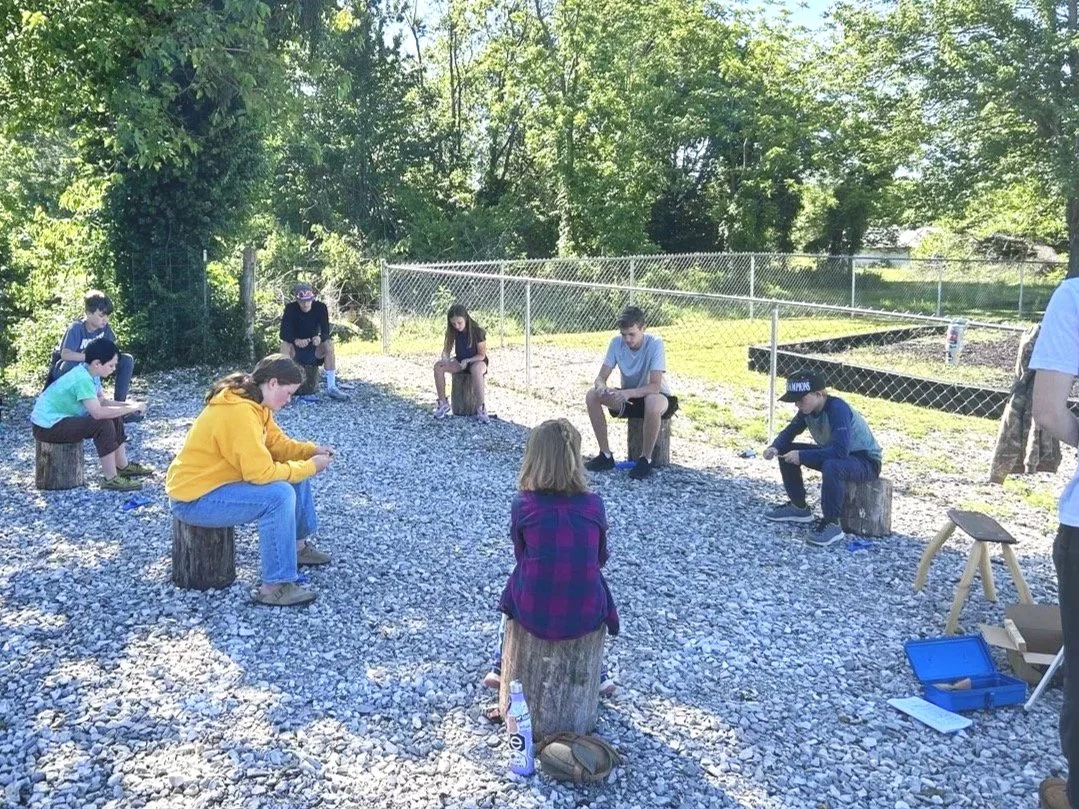 a group of students sitting outside in a circle for a sloyd, wood carving class in Rogers, Arkansas