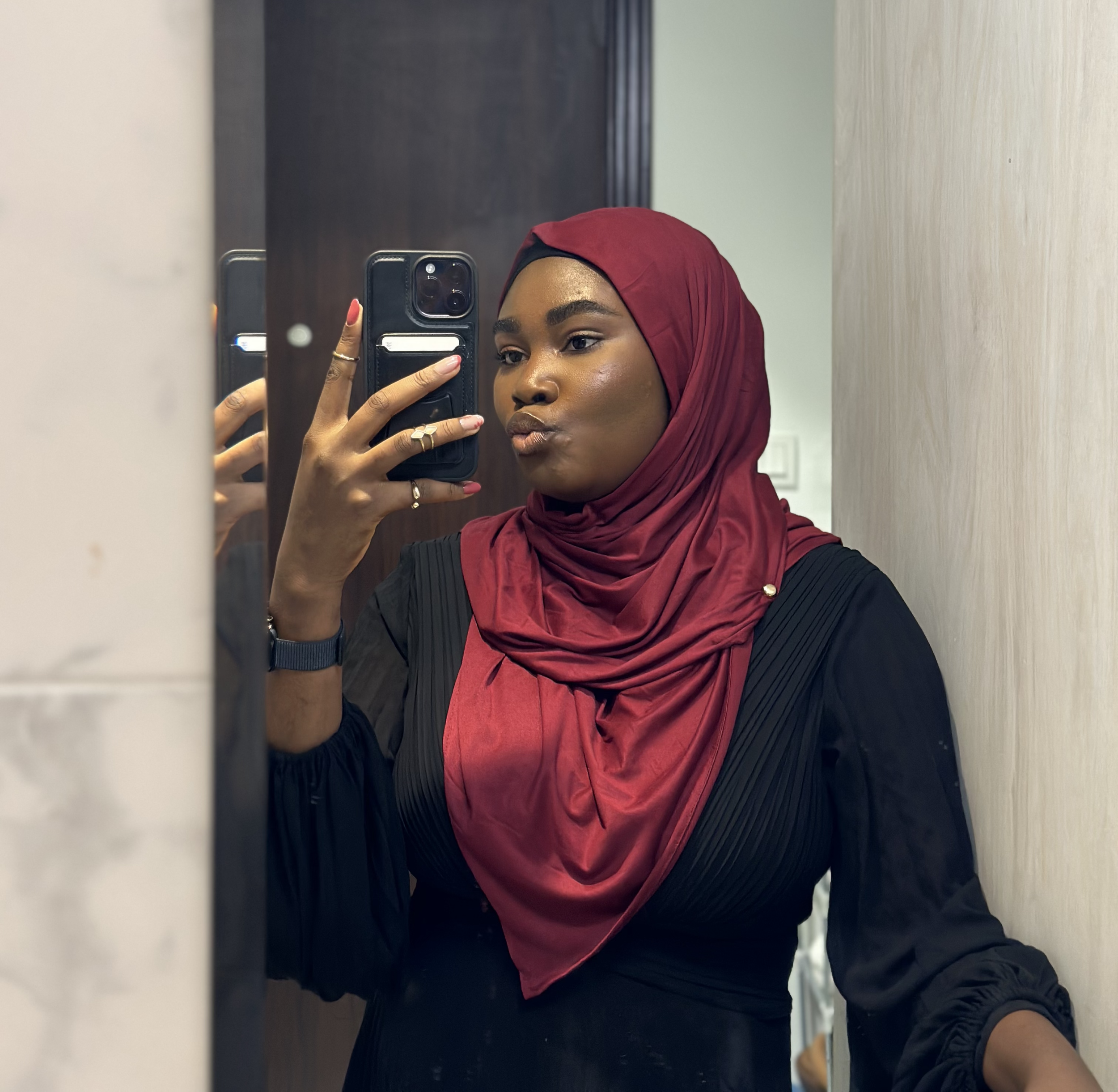 Woman wearing a maroon hijab taking a selfie in front of a mirror.