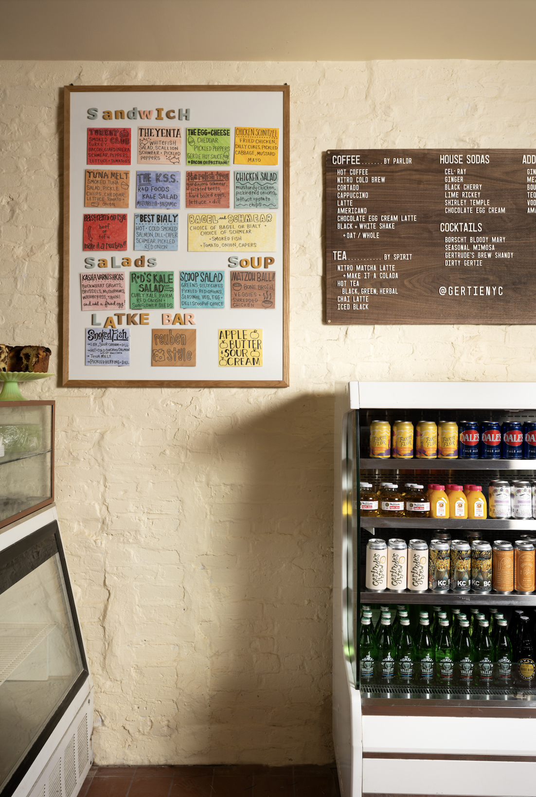 GERTIE interior shot with food and drink menus showcasing bagels, pastries, latkes, salads, etc, as well as a fully stocked drink fridge