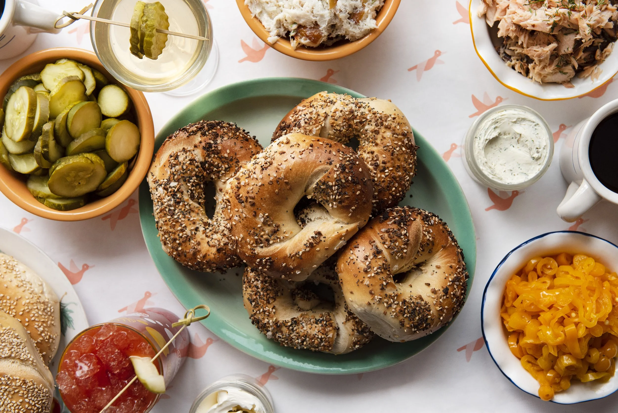 GERTIE brunch spread with bagels topped with bagels, pickles, tuna salad, a cup of coffee, and a martini