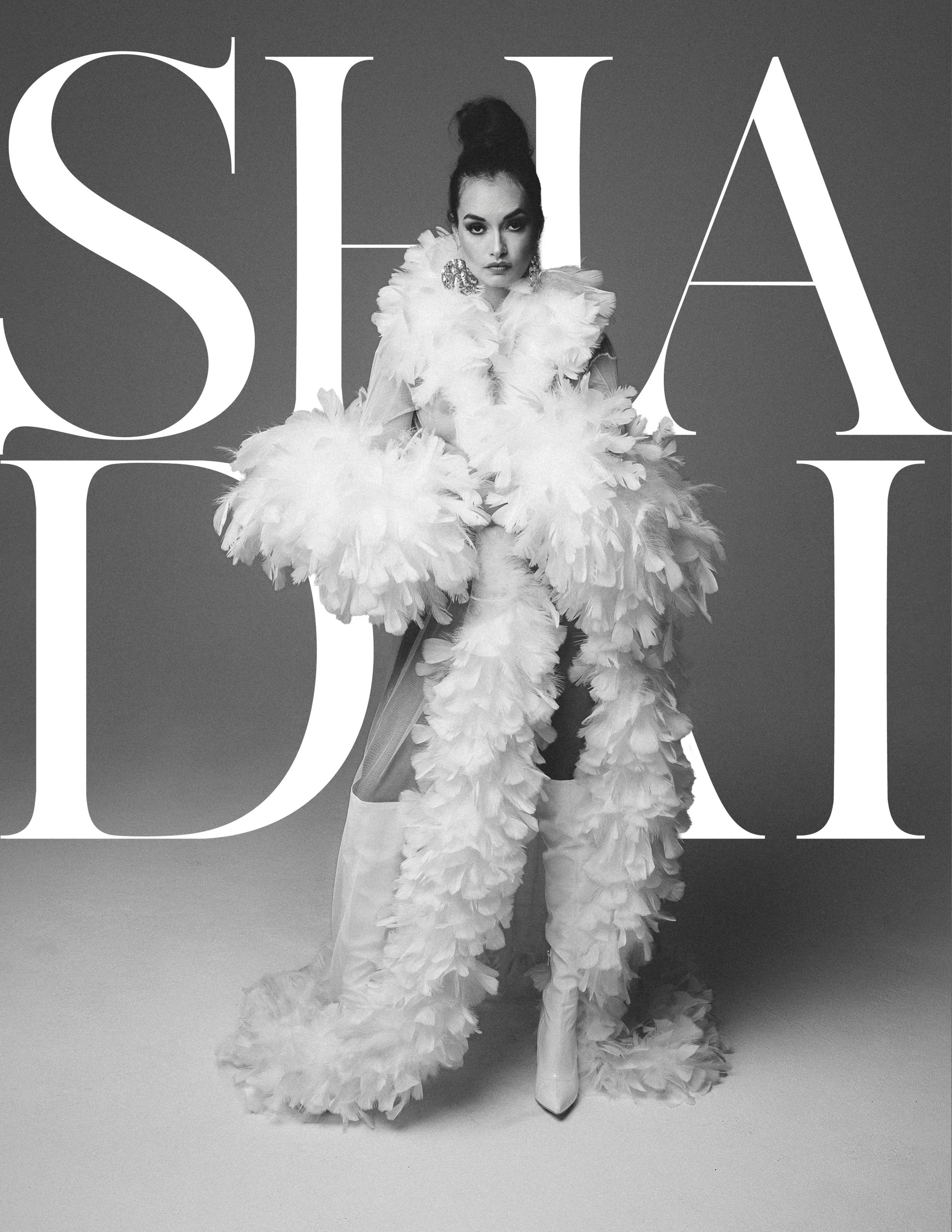 Black and white portrait of a woman in an elaborate feathered outfit, standing against a background with large, stylized text.