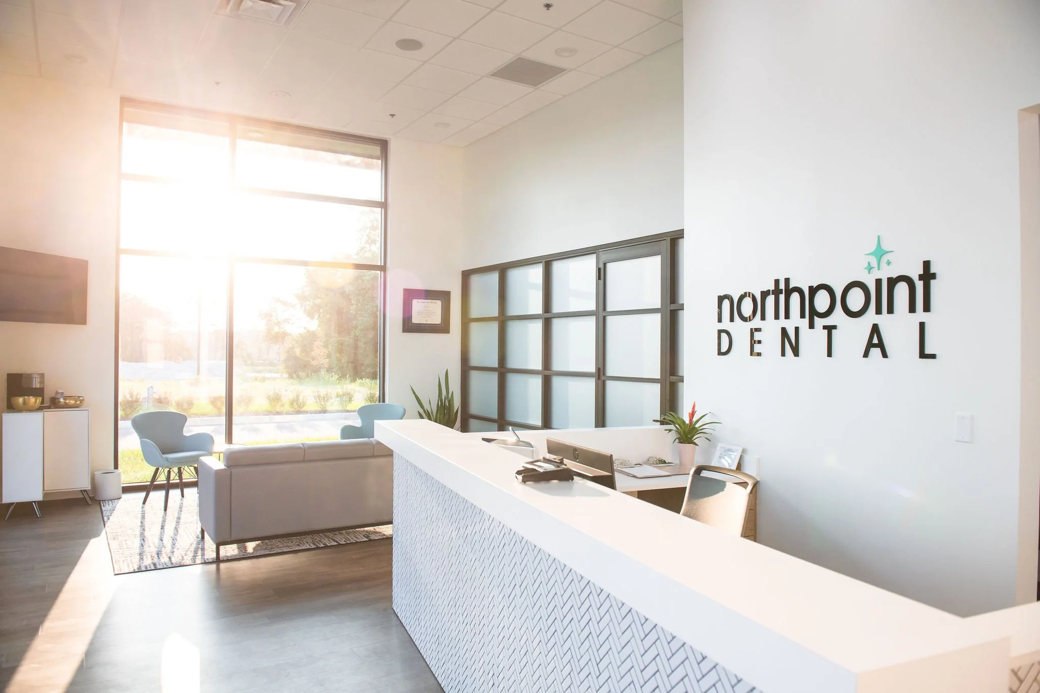 New, clean and visually esthetic interior of Northpoint Dental reception area with bright natural lighting, modern decor, a white counter, and seating area with chairs and a sofa.