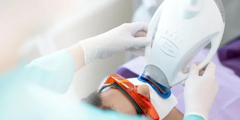 Person undergoing dental or medical procedure with protective goggles, with a healthcare professional adjusting equipment.