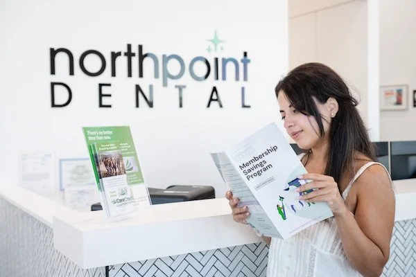 Young woman reading a dental membership plan brochure at the front desk of a dental office in Jacksonville Florida