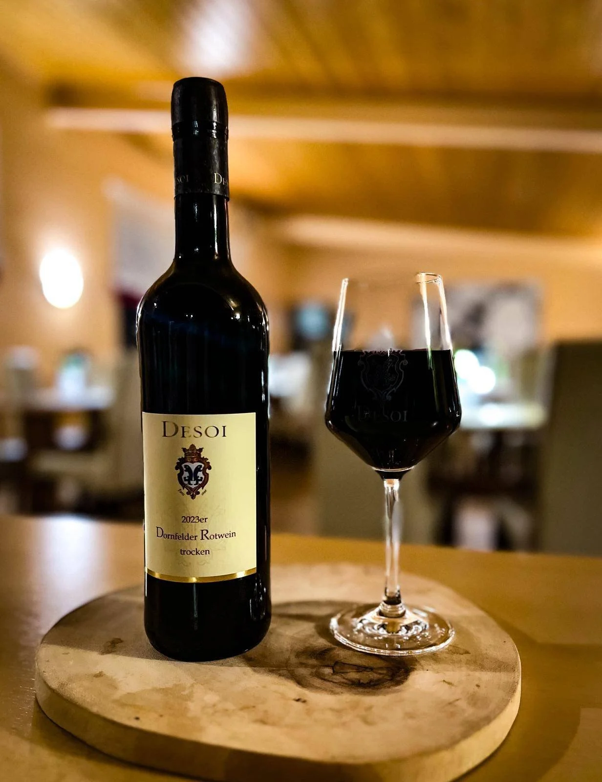 Eine Flasche Rotwein und ein Weinglas mit Rotwein stehen auf einem runden Holzteller auf einem Tisch in einem Restaurant.