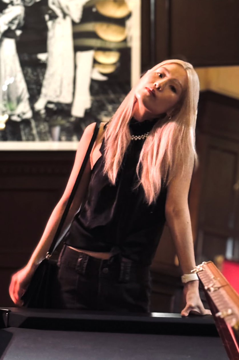 A woman with pink hair leaning on a pool table in a dimly lit room.