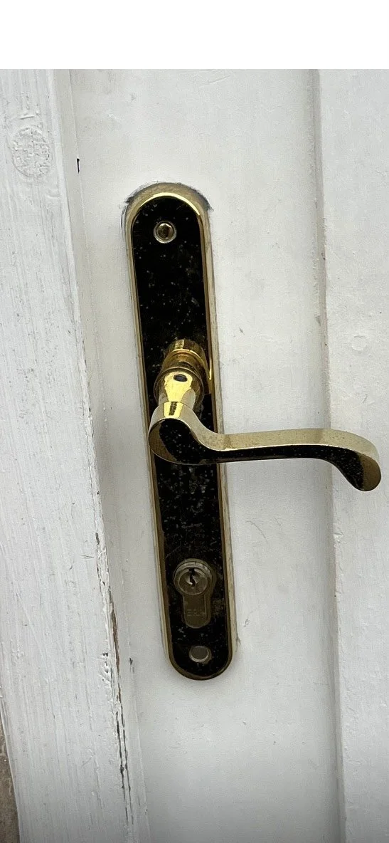 A close-up of a door handle and lock on a white door, with a gold-colored handle and black plate.