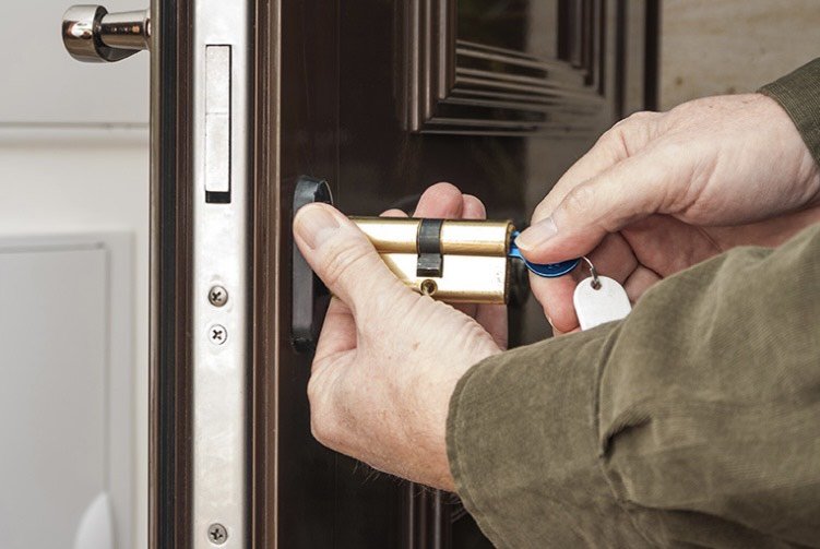 A person inserting a key into a door lock inside a dark wooden door.
