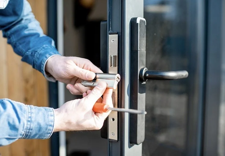 Person installing or repairing a door lock with a screwdriver and a small cylindrical lock component.
