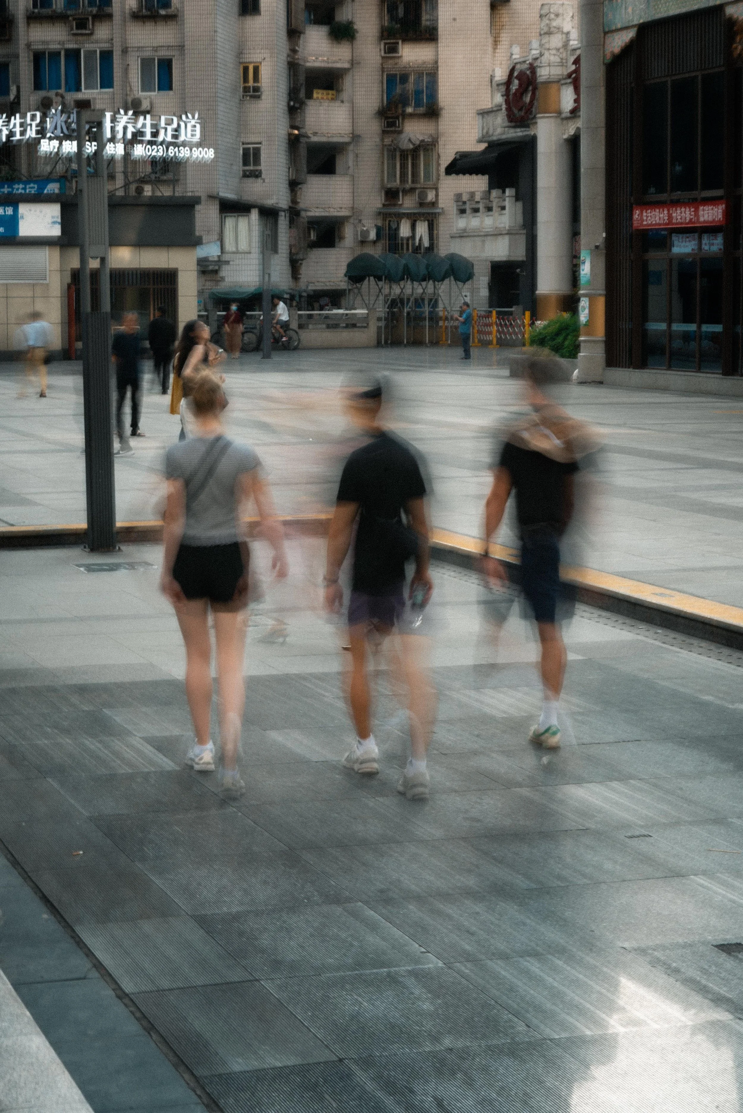 Three people walking on a city sidewalk with motion blur, in front of tall buildings and other pedestrians.