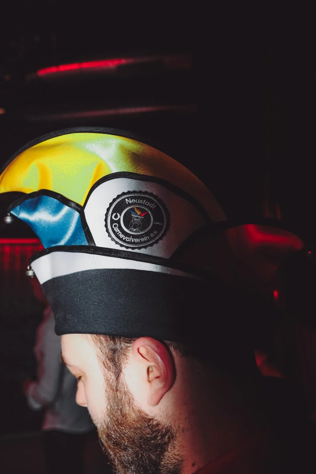 A person with a beard and short hair wearing a helmet with a CAN logo, illuminated in a dim environment.