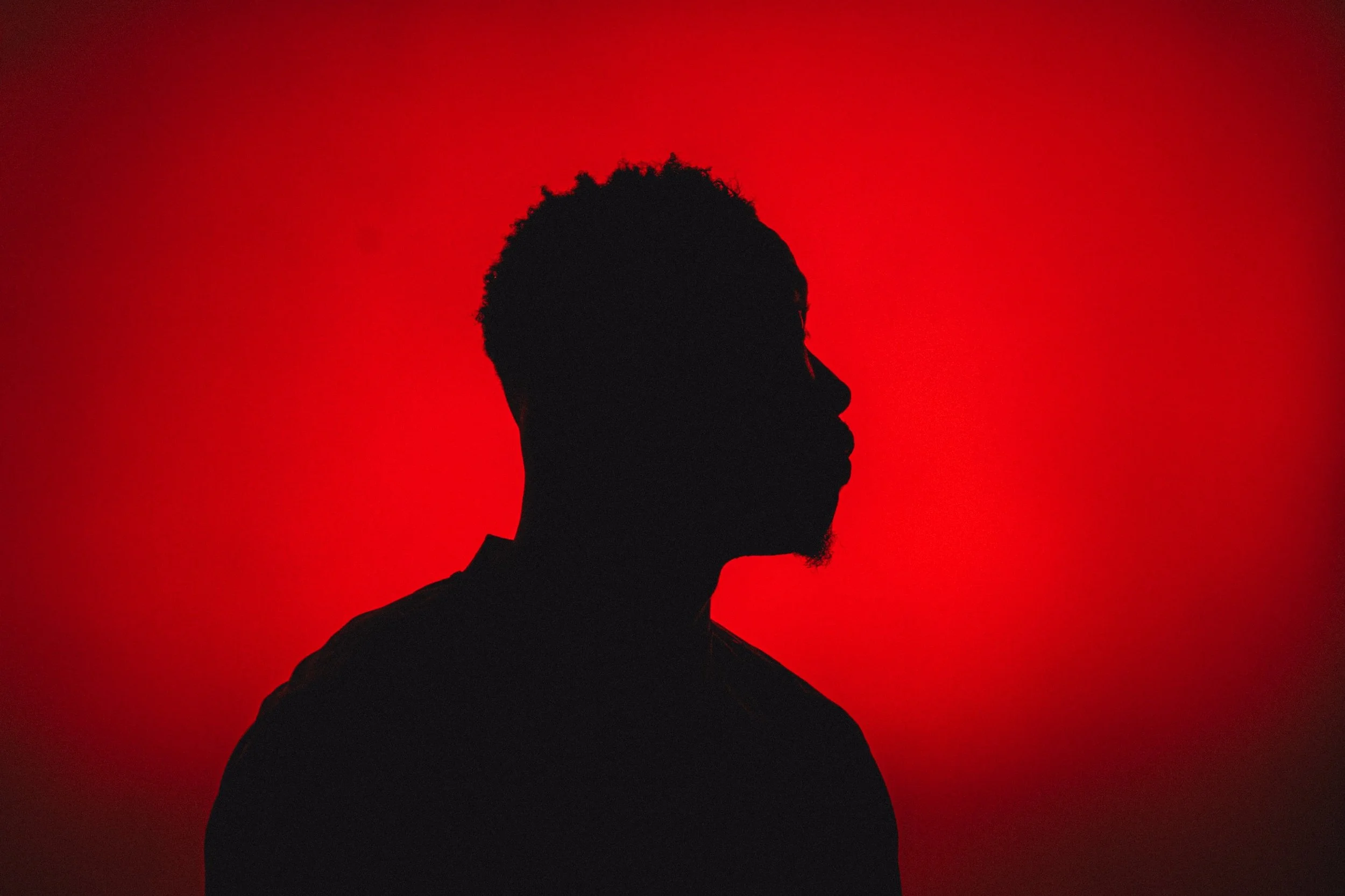 Silhouette of a man with curly hair and glasses against a red background.
