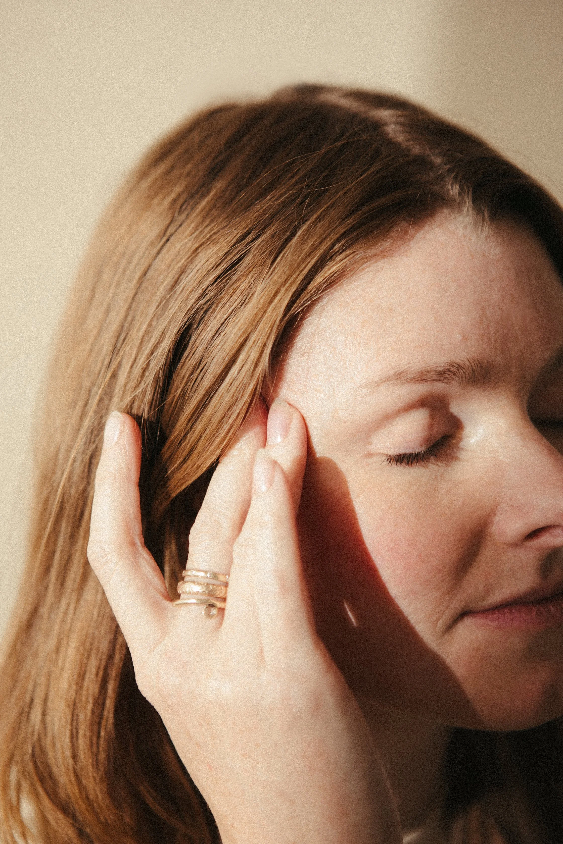 A woman with eyes closed and her finger pressed to her temple.