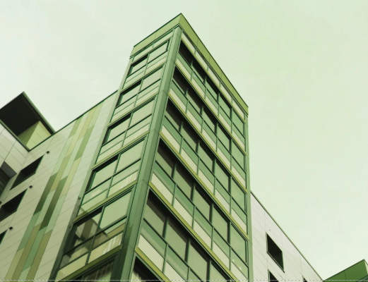 Low-angle view of a modern multi-story building with glass windows and metal framing against a light green sky.