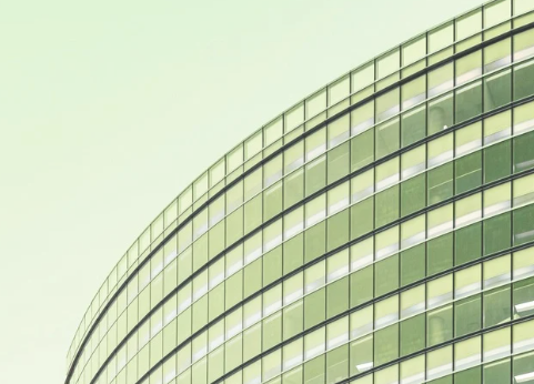 Close-up of a modern glass office building with curved architecture against a light green sky.