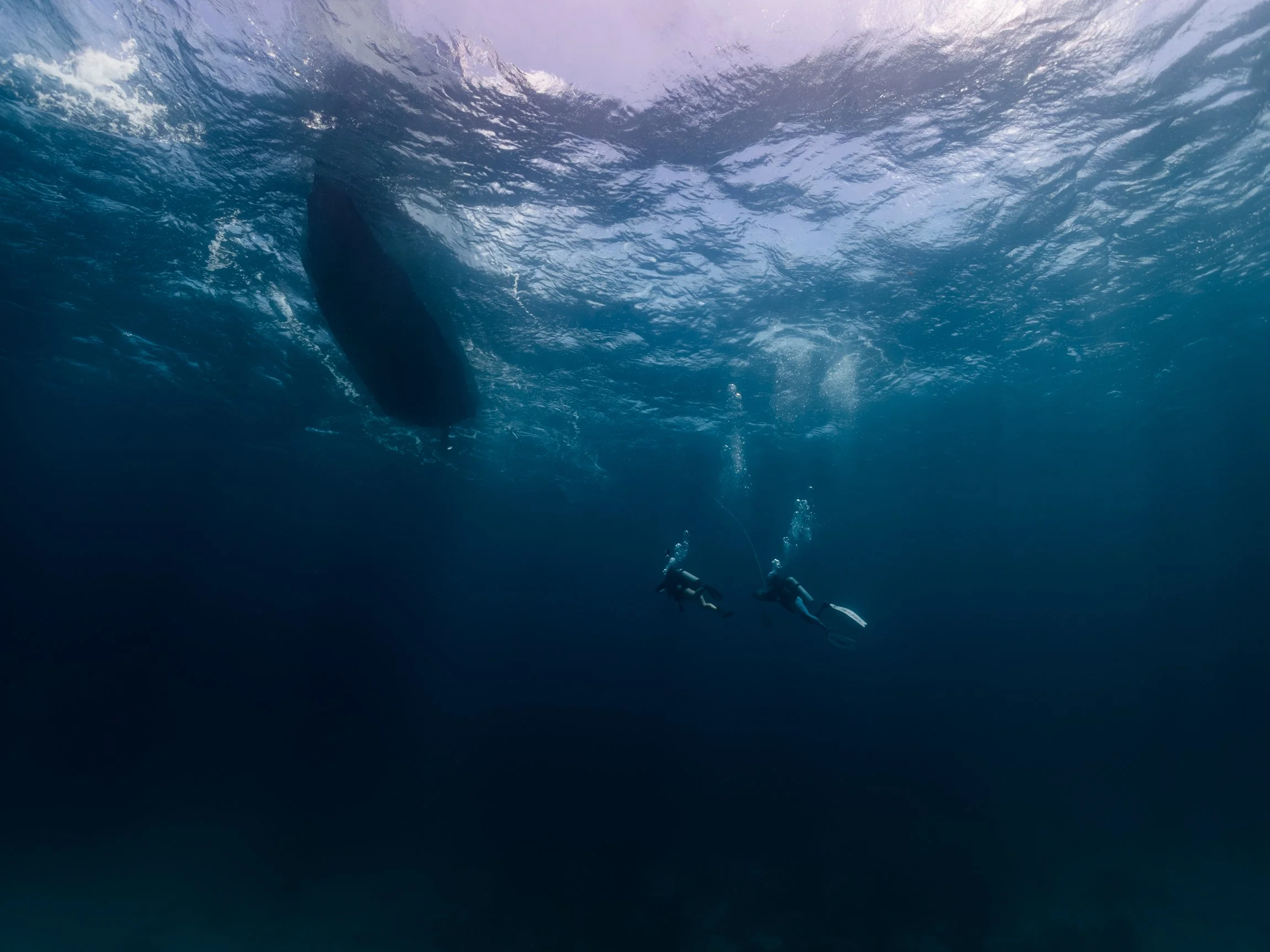 Underwater image of two scuba divers swimming back to the boat to do their safety stop