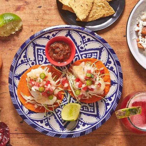 two fresh open face tacos on a colorful blue and white plate with lime and salsa