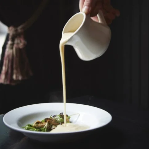 a chef pouring a rich white sauce onto a nicely plated dish