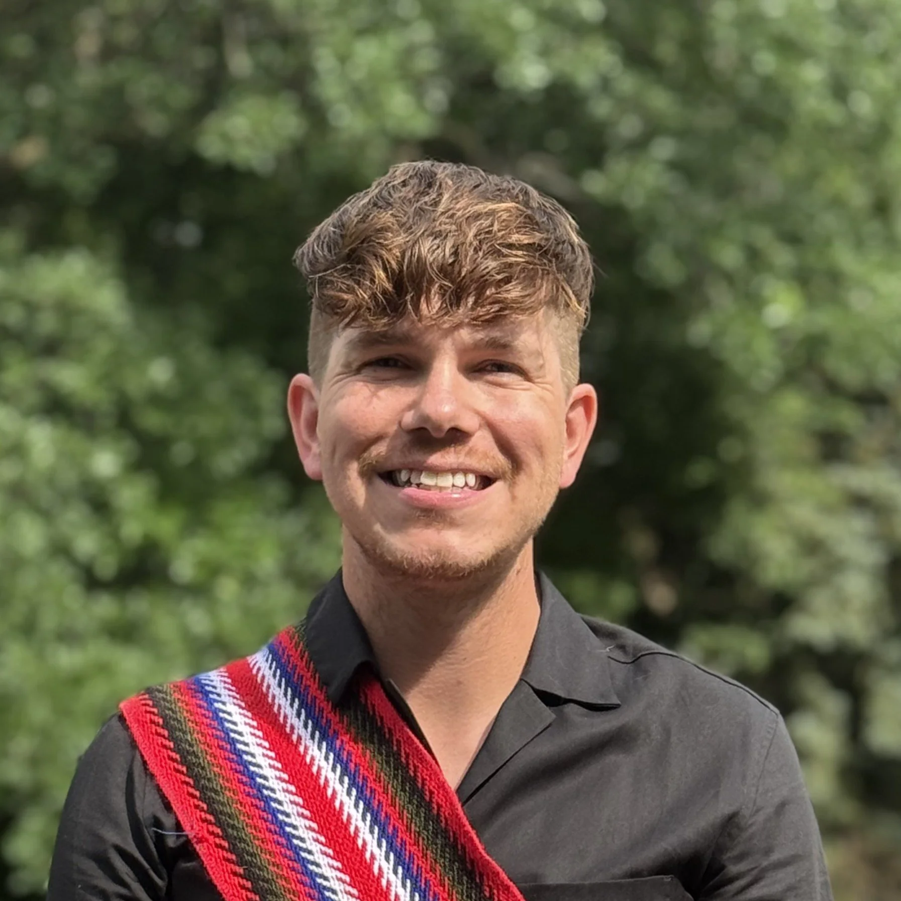 A smiling man with short hair wearing a red Métis sash