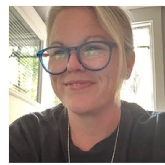 Katie Webb, a smiling woman with blonde hair and glasses, indoors near a bright window.
