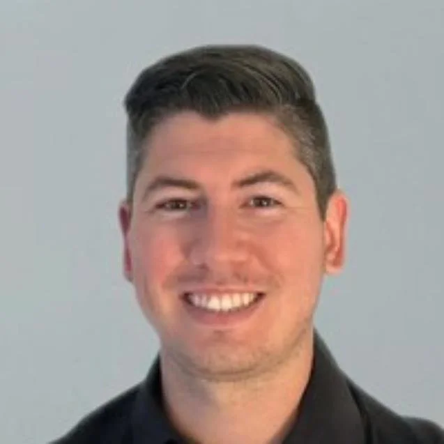 Joshua Drummond, a smiling man with short dark hair wearing a black collared shirt, photographed against a plain grey background.