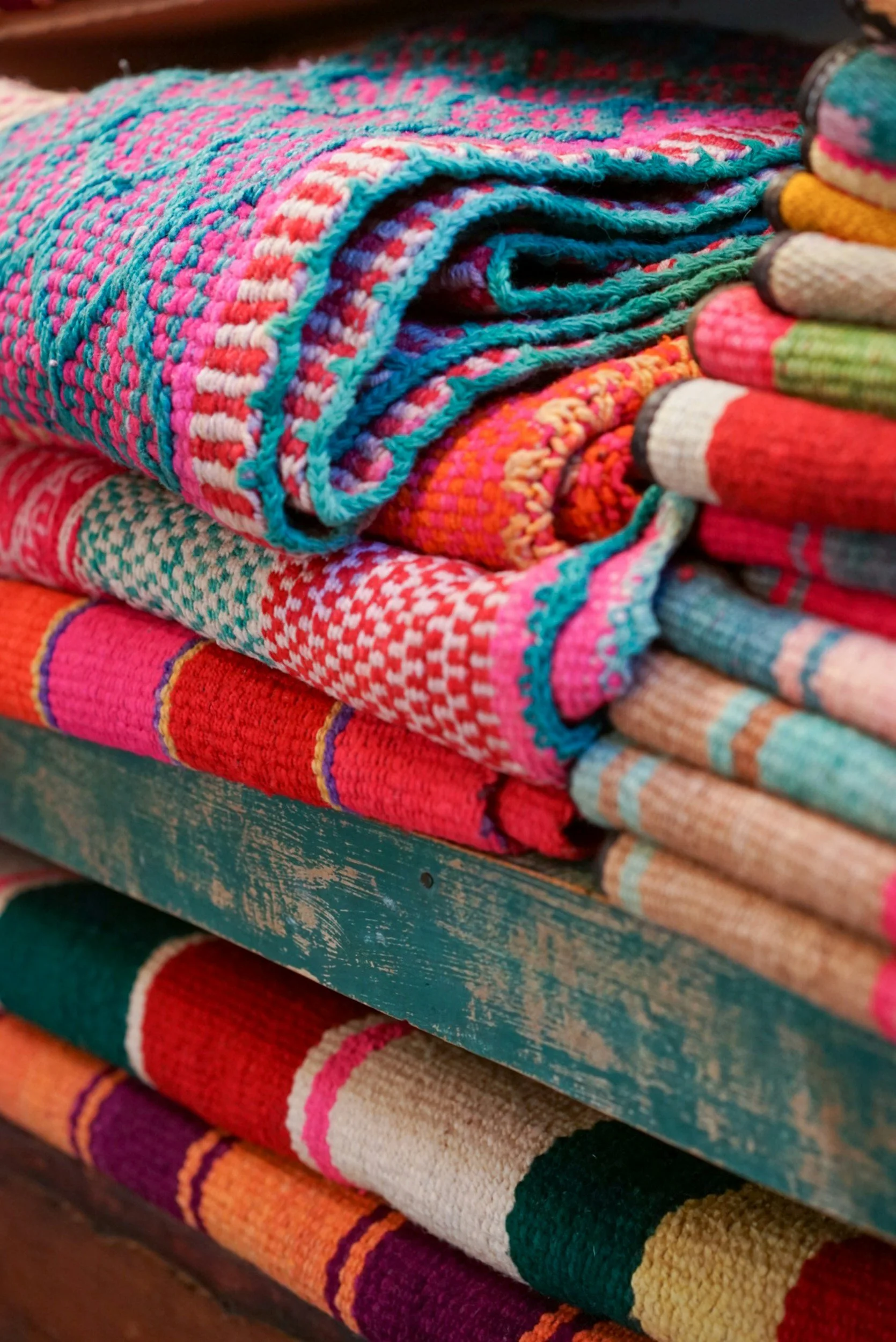 Stacked colorful woven blankets with various vibrant patterns and textures.