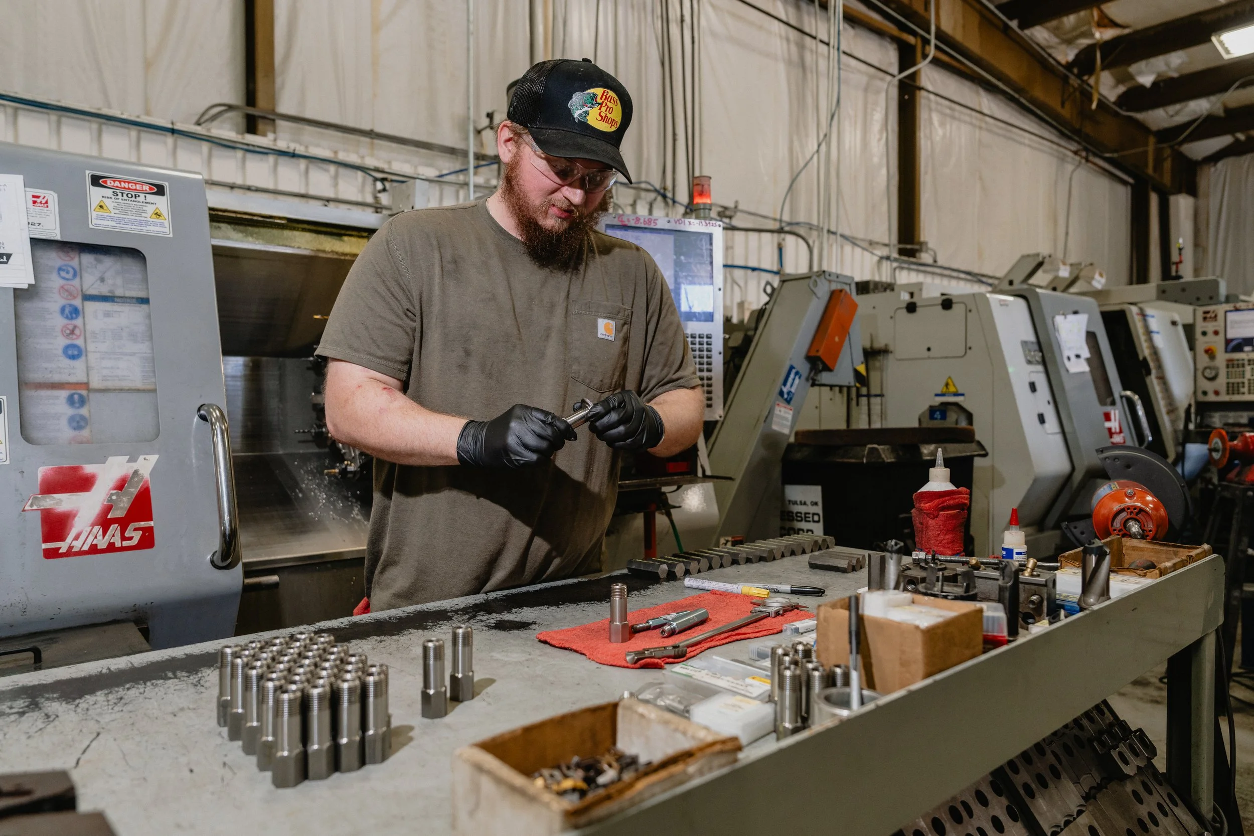 Machinist inspecting a precision turned part at a Haas CNC lathe station in our Tulsa machine shop