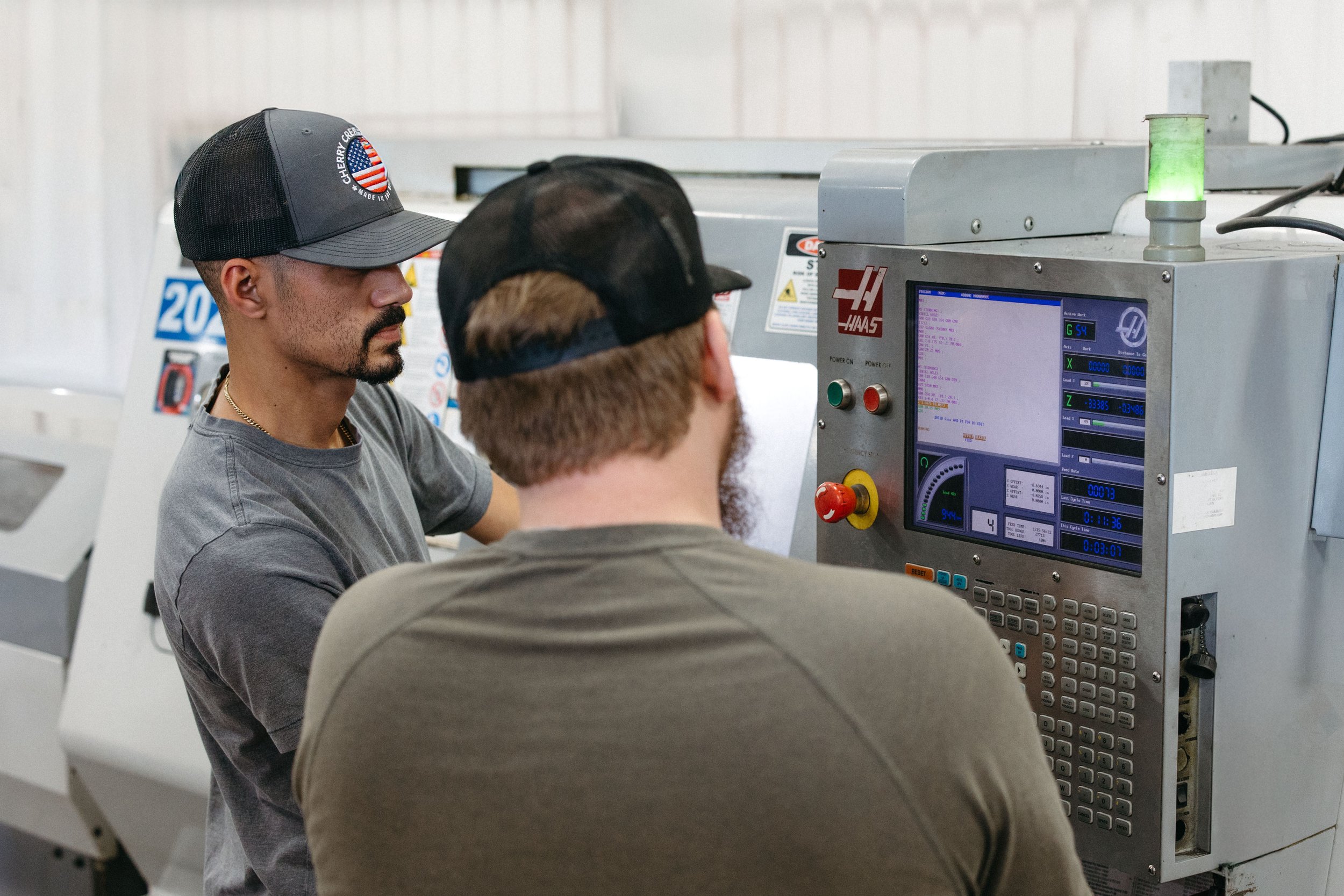 Two men working together at a CNC machine in a factory or workshop.