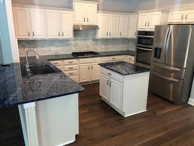 Modern kitchen with white cabinets, dark granite countertops, stainless steel refrigerator, oven, microwave, and a small kitchen island.