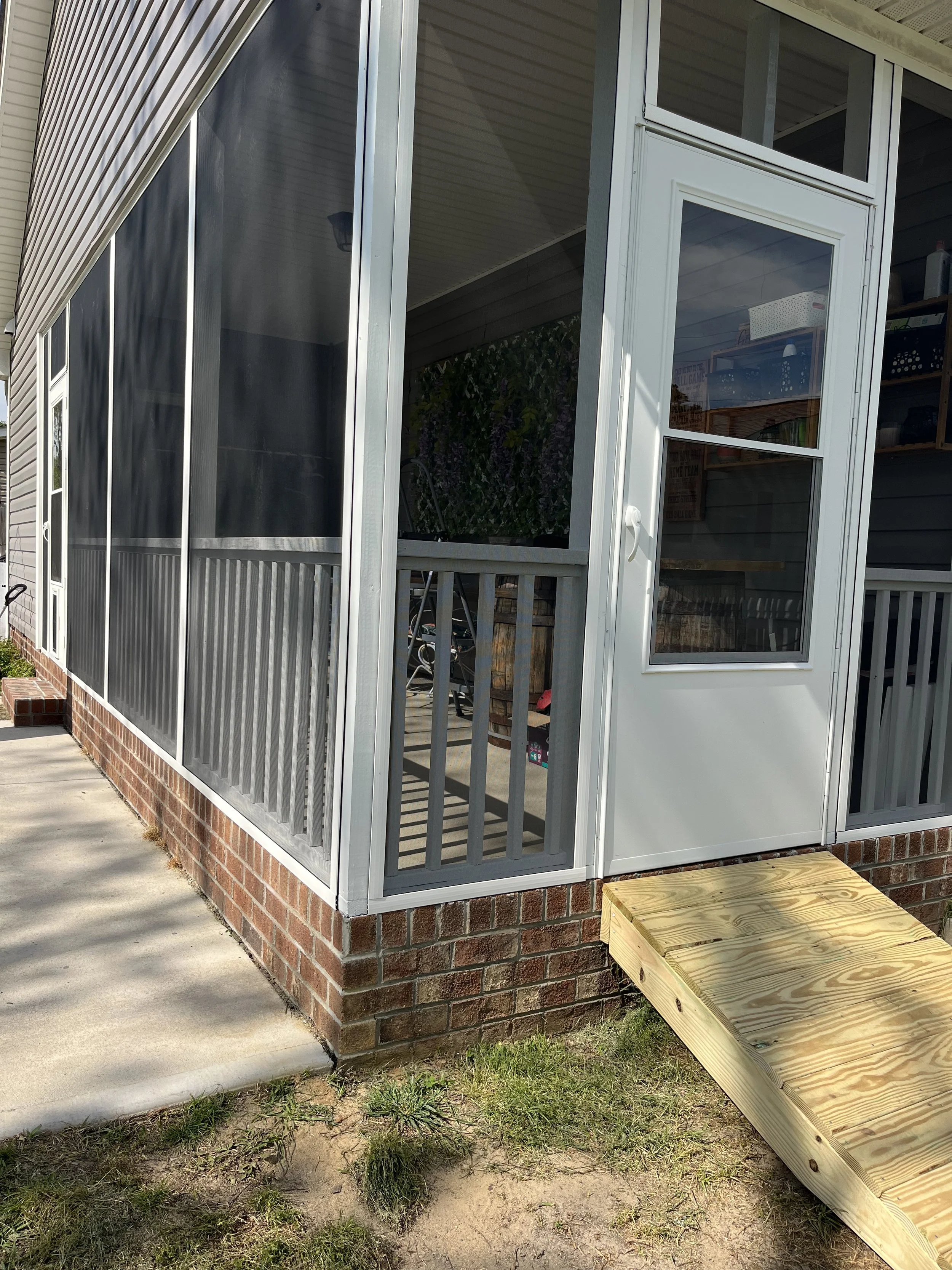 A new screened porch with brick foundation, white framing, and a small wooden ramp at the entrance.