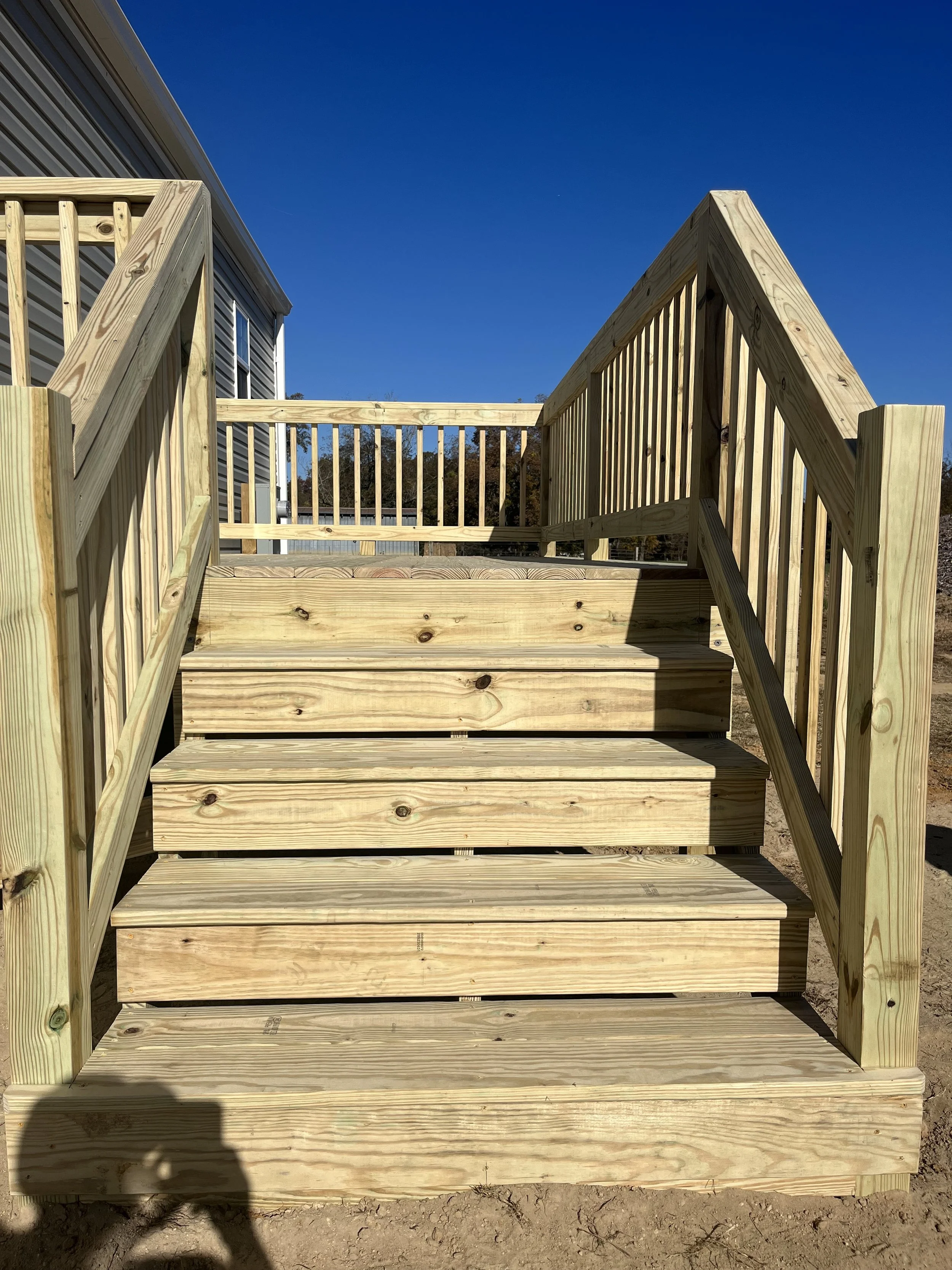 Newly built wooden staircase with railings leading up to a deck attached to a mobile home under a clear blue sky.