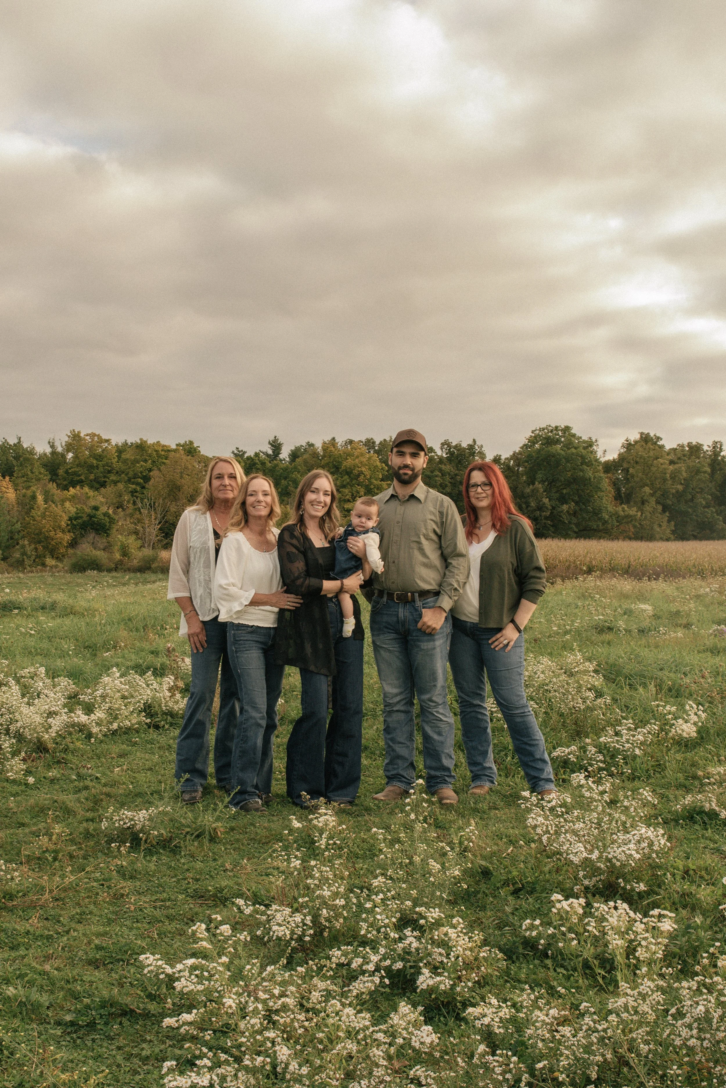 A family of six standing outdoors in a field of white flowers on an overcast day.
