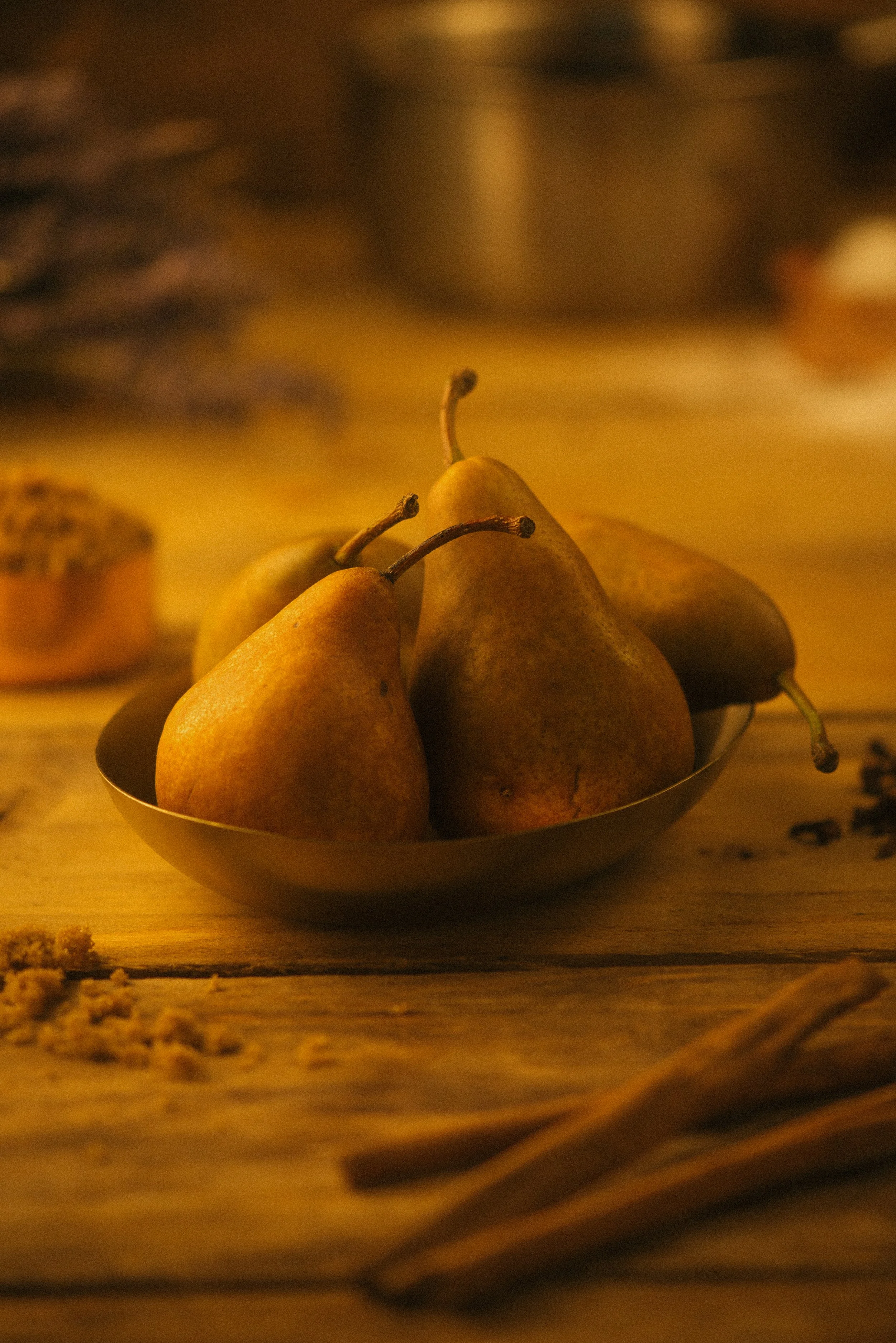 Three ripe yellow pears in a small metallic bowl on a wooden surface with blurred background.