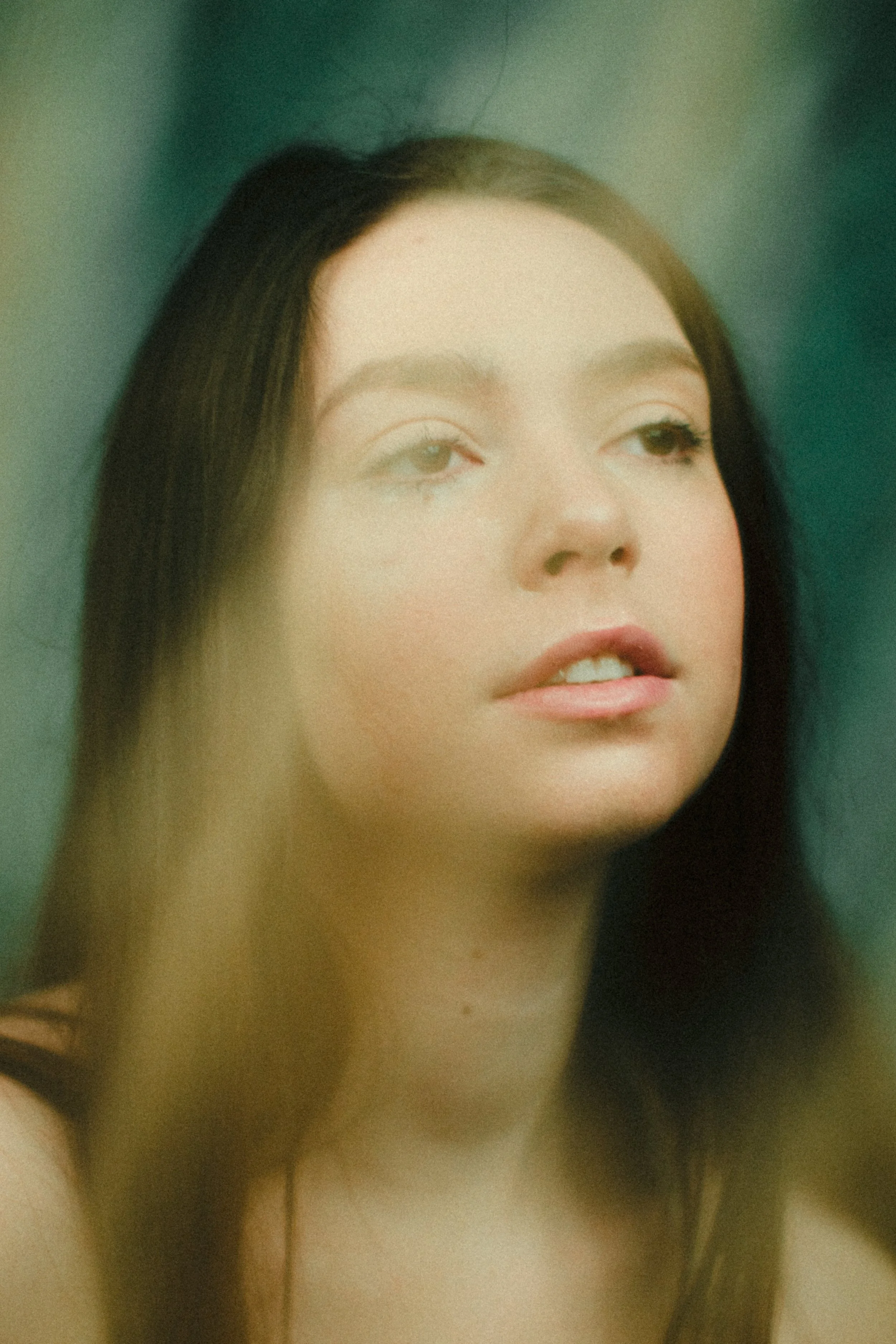 Close-up of a woman with long brown hair looking slightly to the side with a neutral expression.