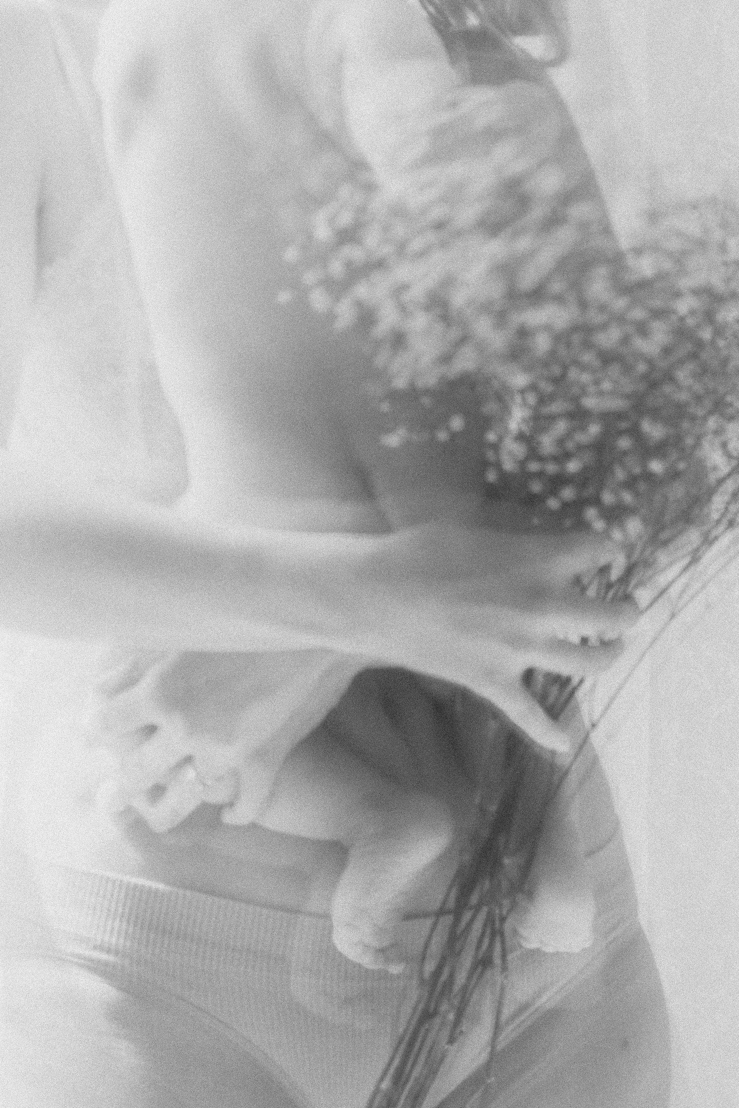 Soft, blurry black and white portrait of a person holding a nude baby with their back to the camera, a bouquet of flowers in the foreground, creating a tender and ethereal atmosphere
