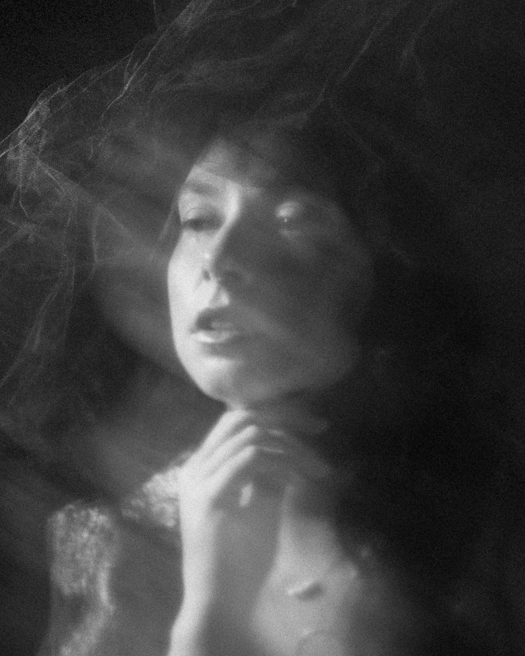 Black and white portrait of a woman with her eyes closed, head slightly tilted, hand resting on her chin, and wisps of hair around her face.