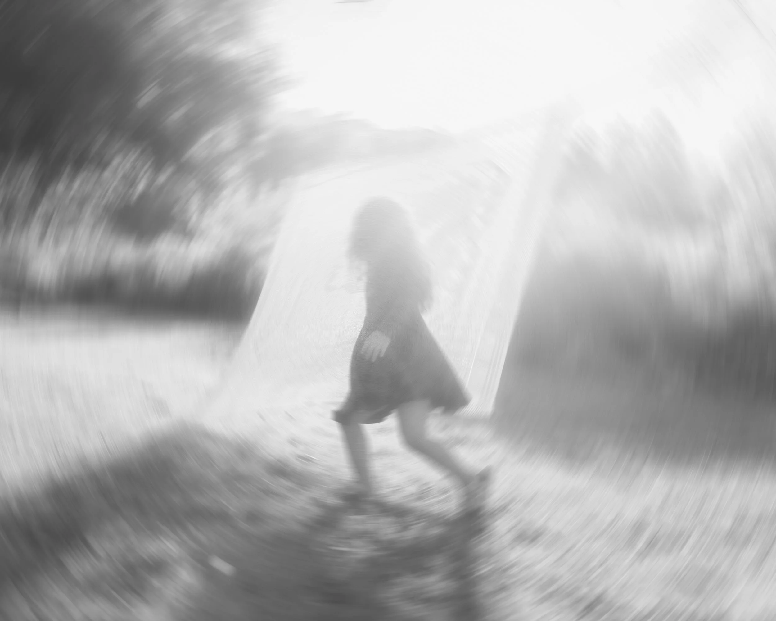 Artistic black and white photograph of a child running outdoors at sunset, backlit with motion blur and soft, high-contrast light, near a large sheet or bed linen hanging on a clothesline, creating a dynamic and ethereal scene