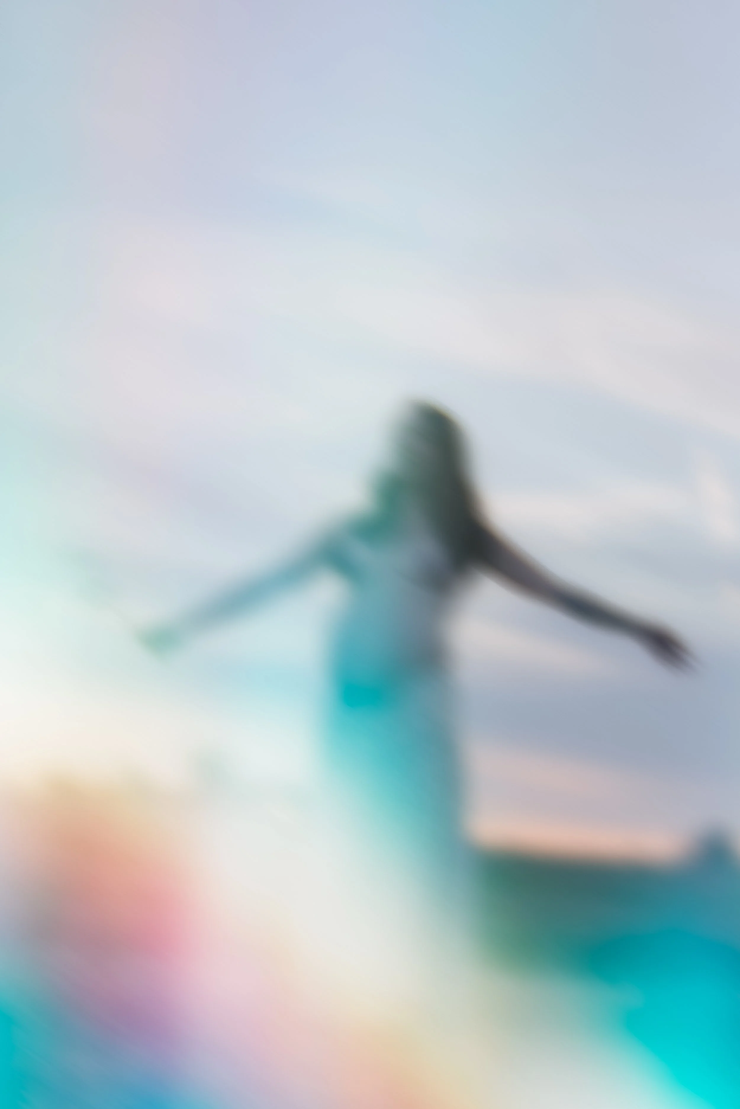 A blurred image of a woman standing outdoors with arms outstretched, against a sky with clouds.