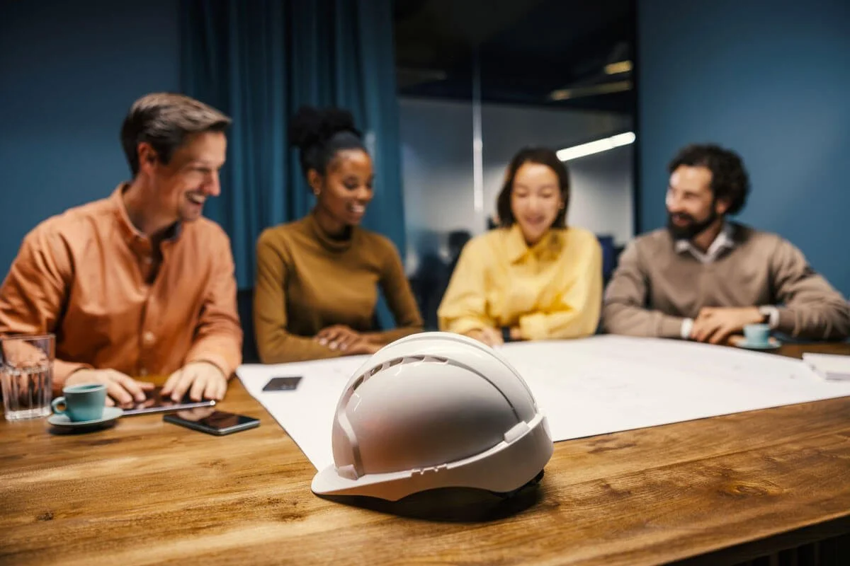 Group of four young professionals collaborating around a table in a bright, modern office with large windows during an elevator consultation.