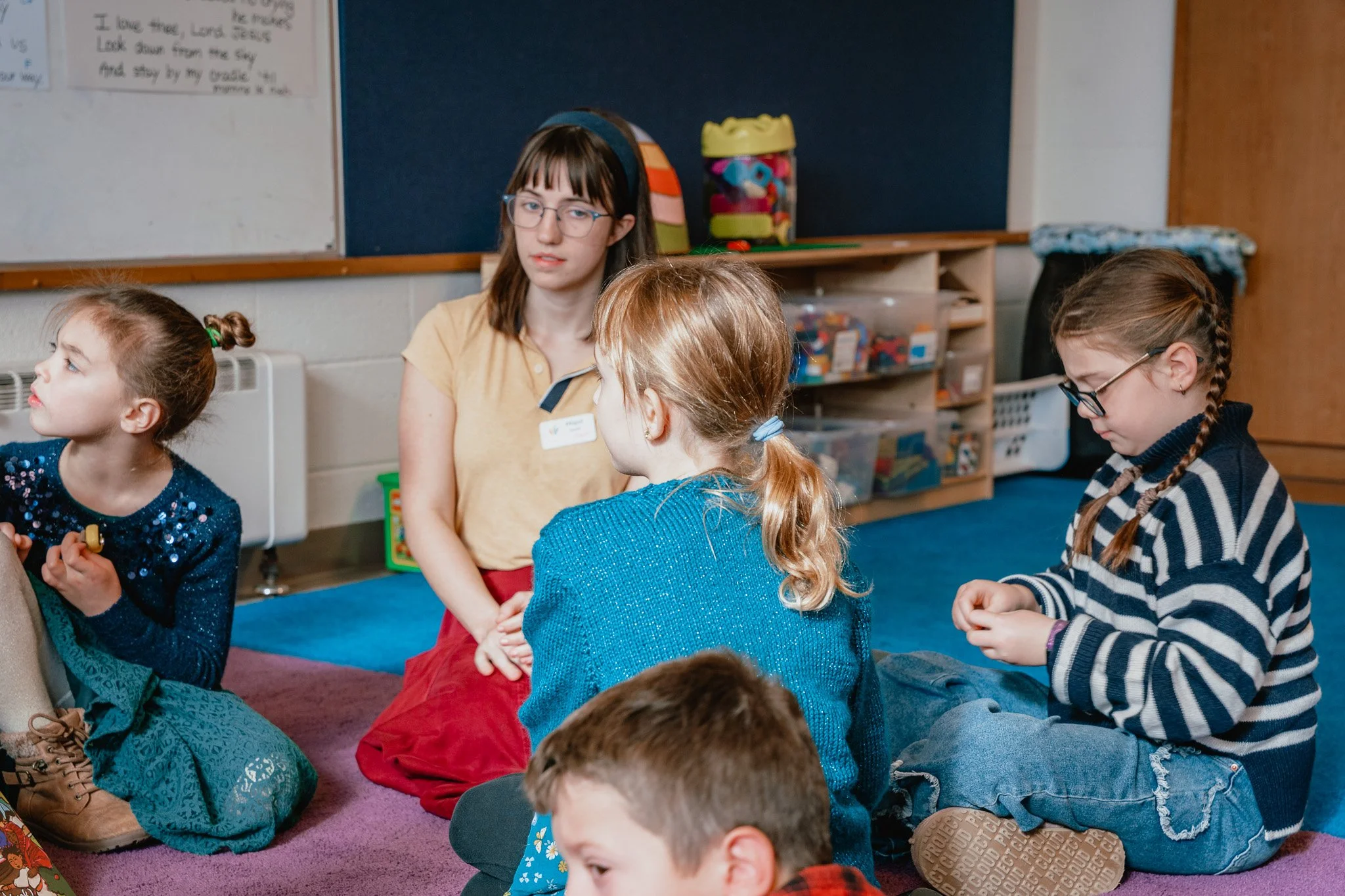 A group of children and a teacher sitting on the floor in a classroom.