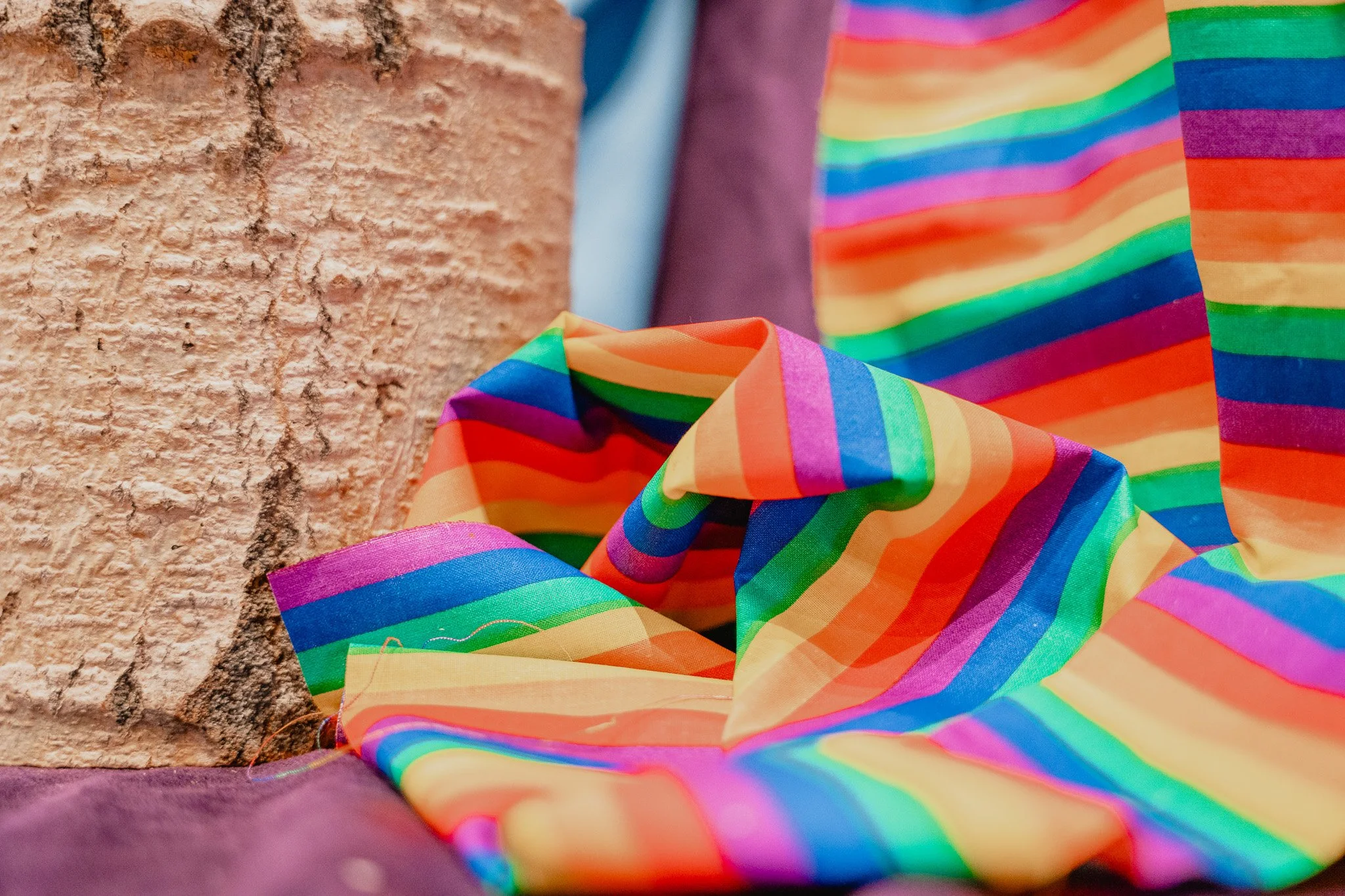 Colorful rainbow striped fabric draped over a brick wall with a purple surface underneath.